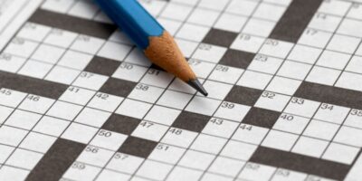 A close-up of an empty crossword puzzle with a pencil lying on top.