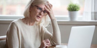 A retired woman looking worried while using a laptop.