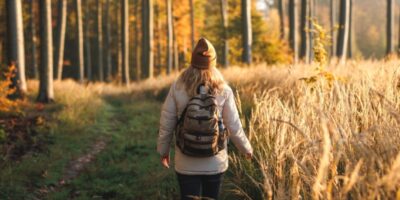A woman with a backpack walking through woodland.