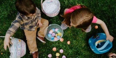 Two children sitting on some grass with Easter eggs and baskets.